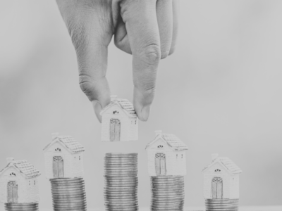 Black and white image of house figures placed on top of stacks of coins